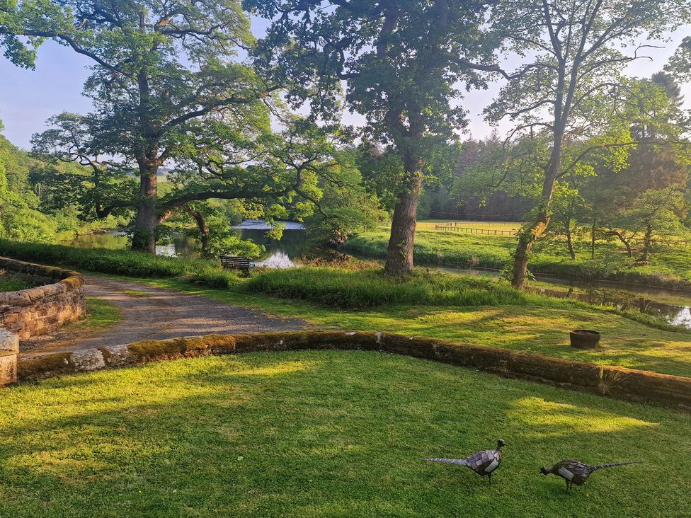 A garden with trees and a river at Romsey Lodge in Wark