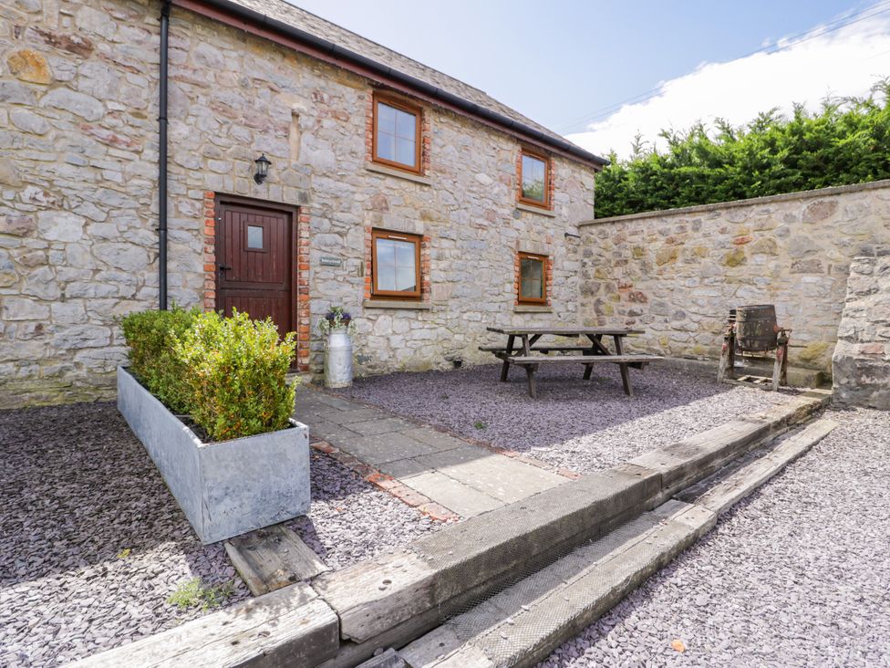 An outdoor area with a stone building, table, and seating at Stabal-y-Gwedd in Dolwen near Abergele