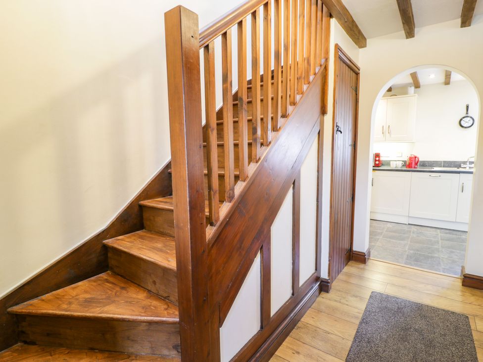 A hallway with wooden stairs and a doorway to the kitchen at Beudy Bach in Dolwen near Abergele