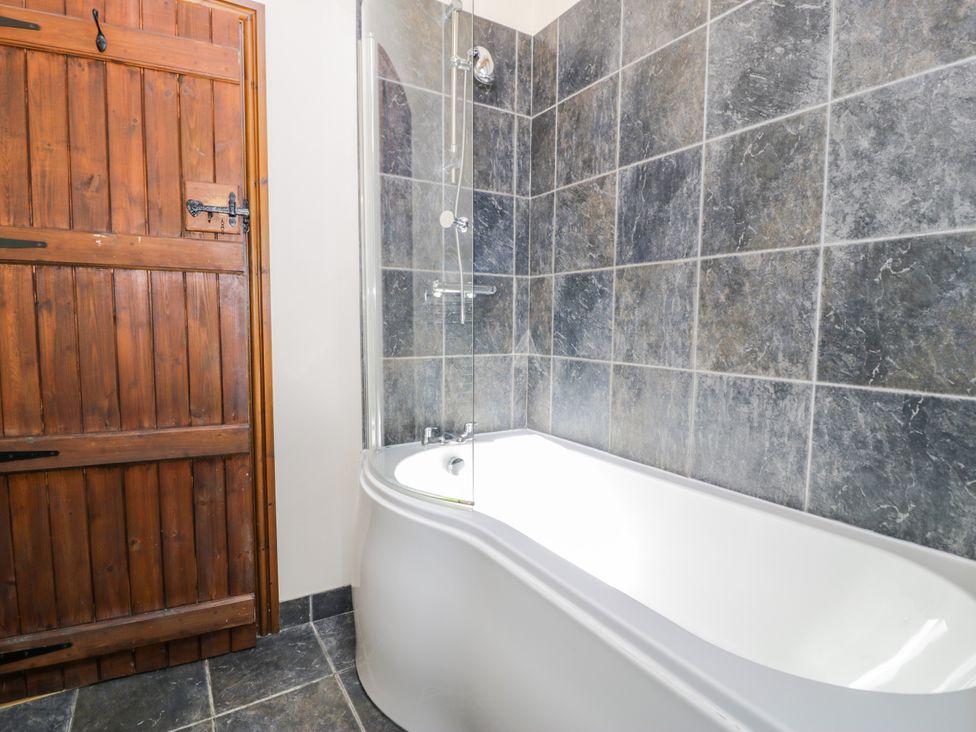 A bathroom featuring a bathtub and shower with a wooden door at Beudy Bach Dolwen near Abergele