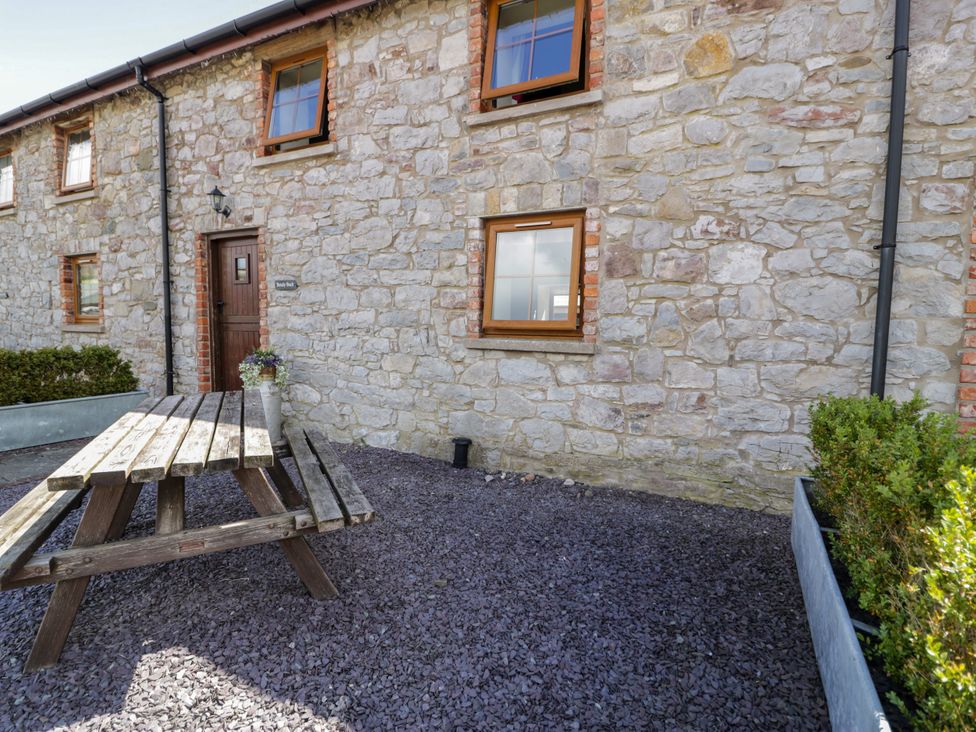 An outdoor area with stone walls and a wooden table at Beudy Bach Dolwen near Abergele