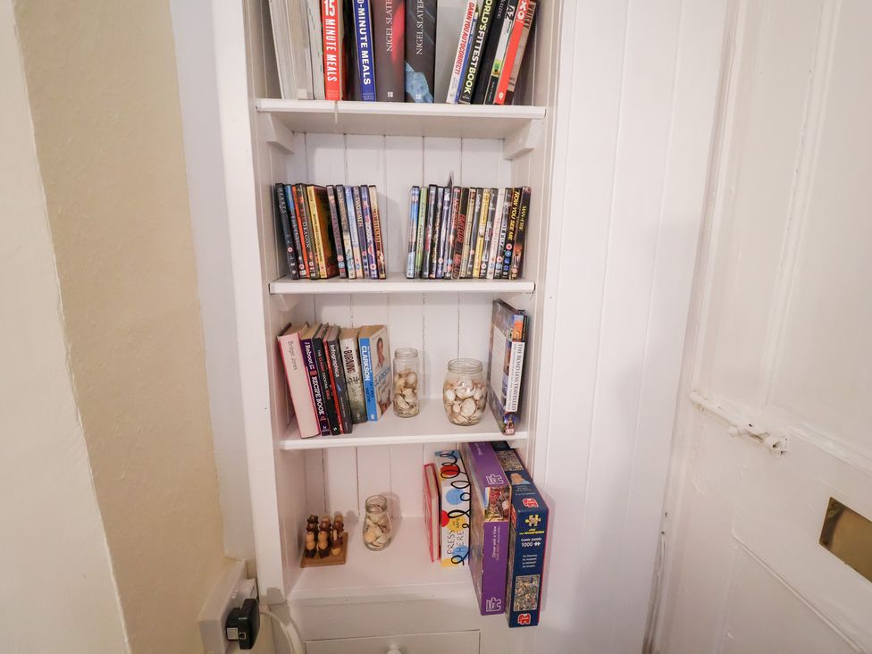 A living room shelf with books and dvds at Cobbler's Cottage in Mundesley