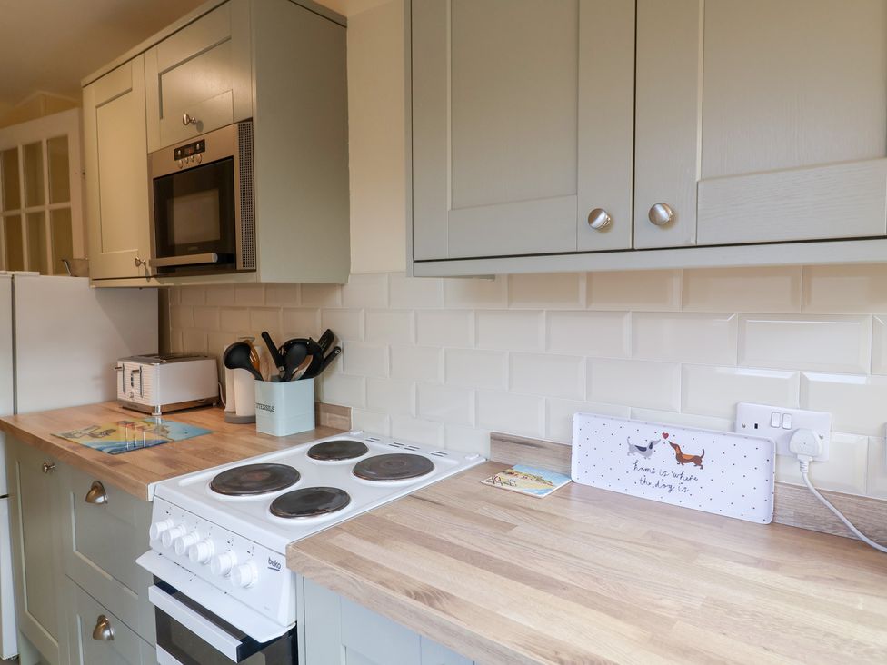 A kitchen with a cooking stove and microwave at Cobbler's Cottage Mundesley