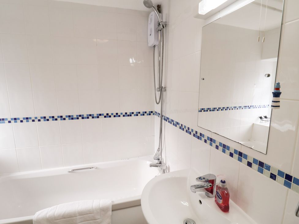 A bathroom with a bathtub, shower, and sink at Cobbler's Cottage Mundesley