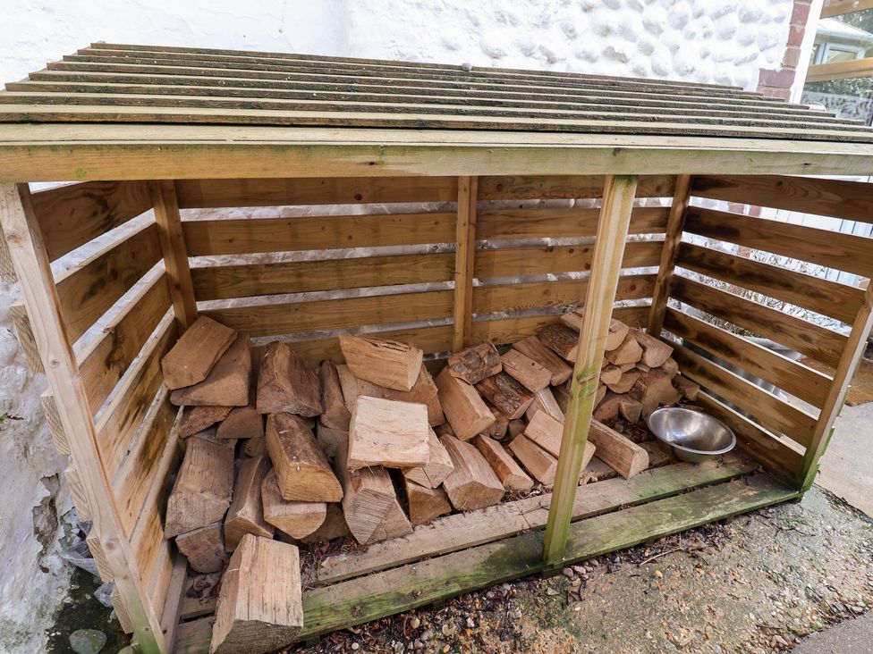 A wood storage shed filled with firewood and a metal bowl at Cobbler's Cottage Mundesley