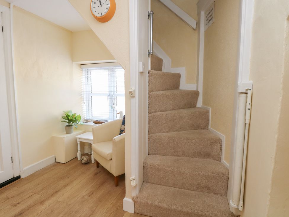 A hallway with a staircase, chair, table, and plant at Cobbler's Cottage in Mundesley