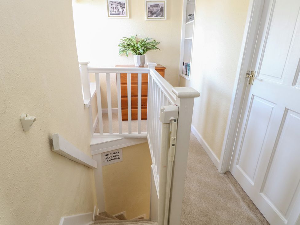 A staircase with a handrail and a chest of drawers in a hallway at Cobbler's Cottage Mundesley