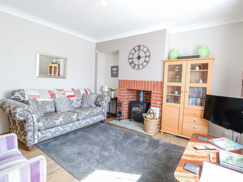 A living room with a patterned sofa a wood burning stove a wooden cabinet and a television at Lillies Pad in Methwold near Feltwell