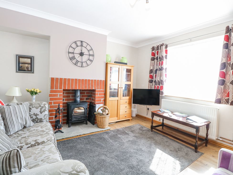 A living room with a floral sofa a brick fireplace a wall clock a TV on a wooden stand and patterned curtains at Lillies Pad Methwold near Feltwell