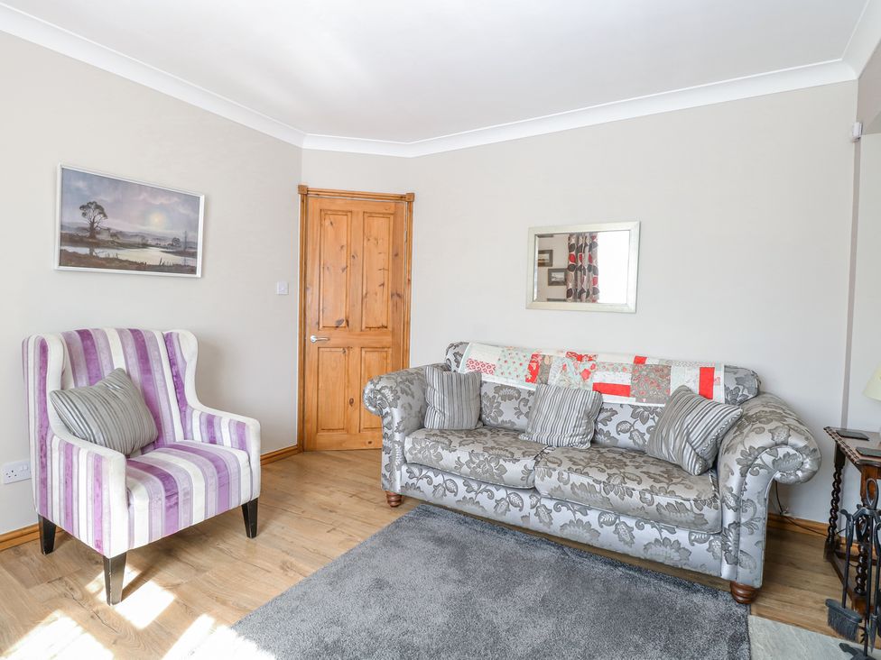 A living room with a striped armchair a floral sofa a wooden door and a landscape painting at Lillies Pad in Methwold near Feltwell