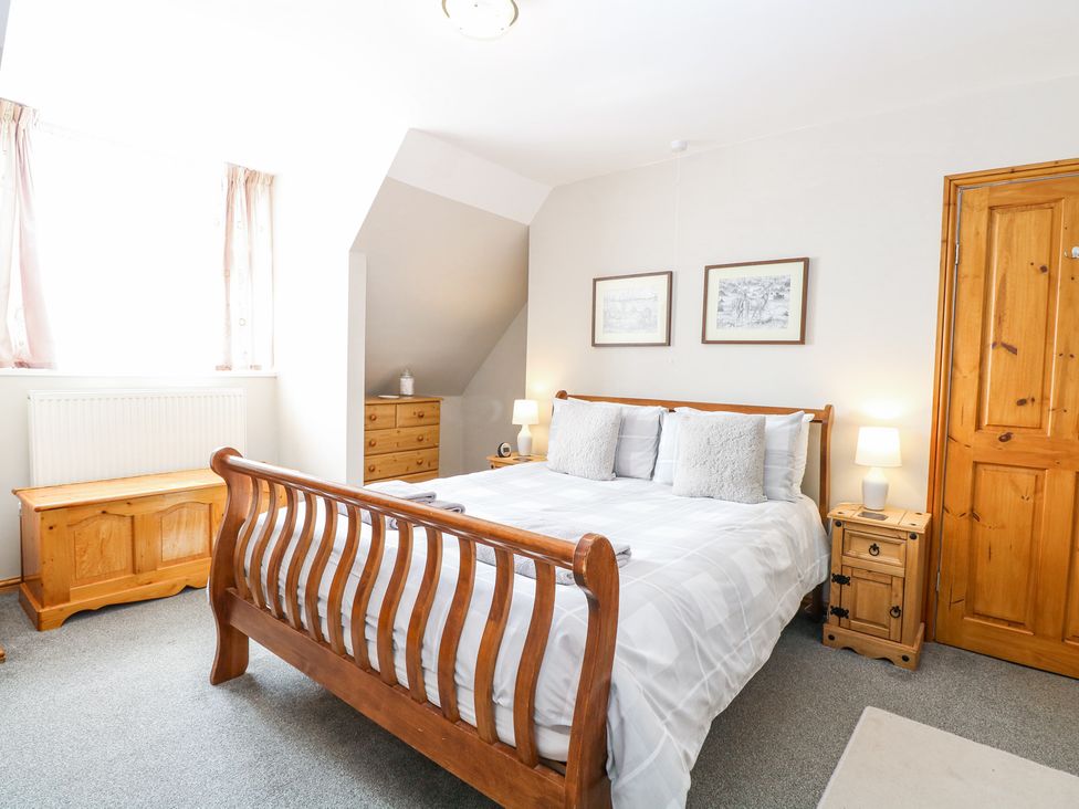A bedroom with a wooden bed frame bedside tables with lamps a chest of drawers and a wooden storage bench at Lillies Pad in Methwold near Feltwell