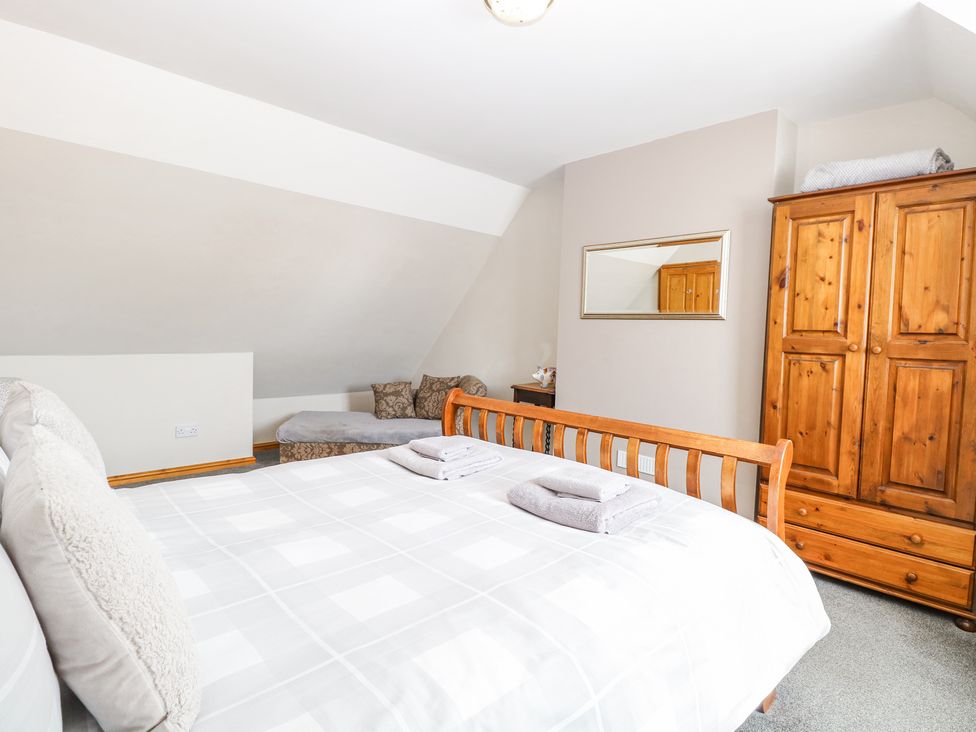 A bedroom with a wooden bed, folded towels, a wooden wardrobe, a chaise lounge with cushions, and a mirror on the wall at Lillies Pad in Methwold near Feltwell