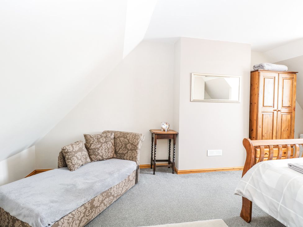 A bedroom with a wooden bed frame a padded daybed a wooden wardrobe a small table and a wall mirror at Lillies Pad Methwold near Feltwell
