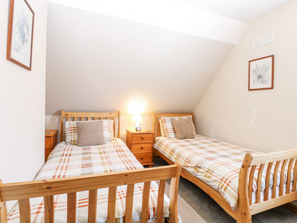 A bedroom with two single wooden beds a small wooden nightstand with a lamp and framed pictures on the walls at Lillies Pad in Methwold near Feltwell