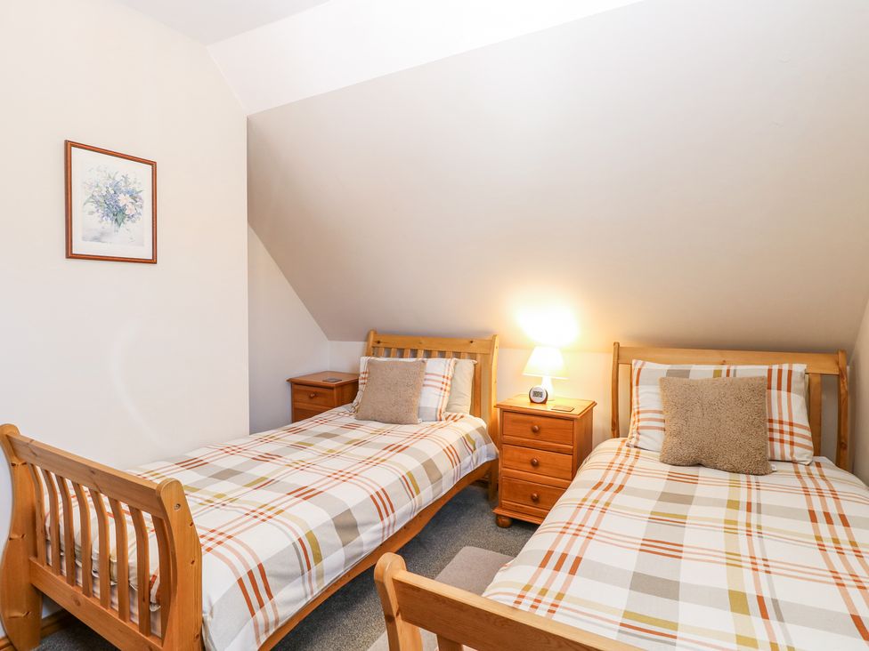 A bedroom with two wooden single beds with checked bedding a nightstand with a lamp and a clock and a framed picture on the wall at Lillies Pad in Methwold near Feltwell