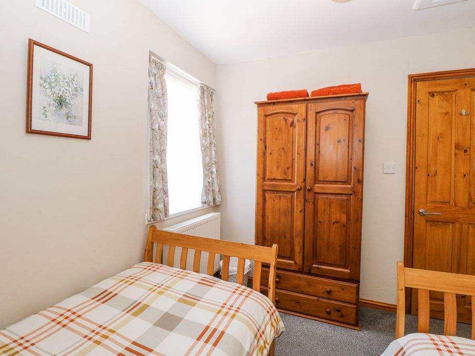 A bedroom with two wooden beds a wooden wardrobe a wooden door and a window with curtains at Lillies Pad in Methwold near Feltwell