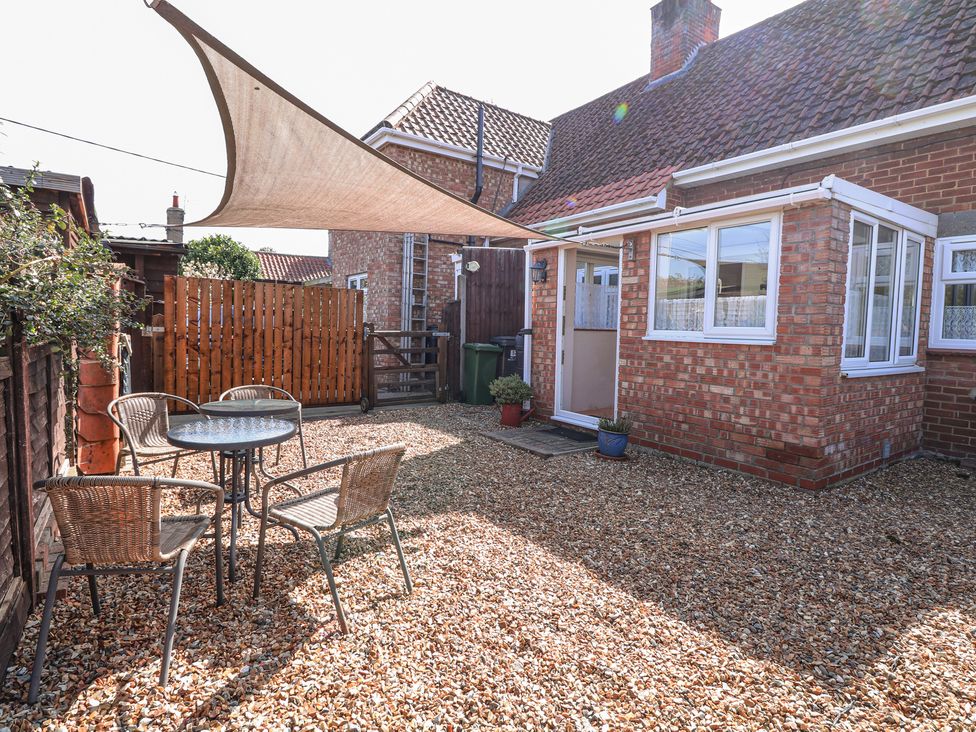 A backyard with a gravel ground four chairs and a round glass table under a sunshade at Lillies Pad in Methwold near Feltwell
