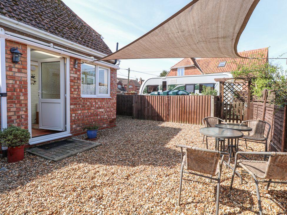 An outdoor patio area with gravel ground shading sail two glass tables and wicker chairs at Lillies Pad in Methwold near Feltwell
