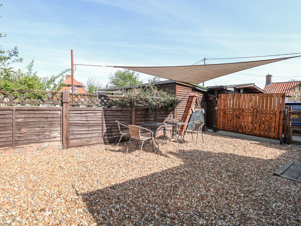 A gravel patio area with three metal chairs around two small round tables under a shade sail at Lillies Pad in Methwold near Feltwell