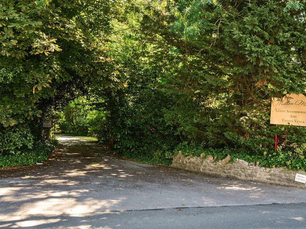 A pathway leading through trees with a sign at Milton Manor in Milton On Stour