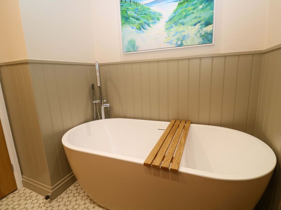 A bathtub with a wooden tray and a painting on the wall at The Poop Deck in Coverack
