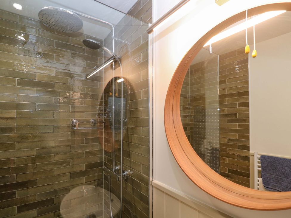 A bathroom with a shower and a round mirror at The Poop Deck in Coverack
