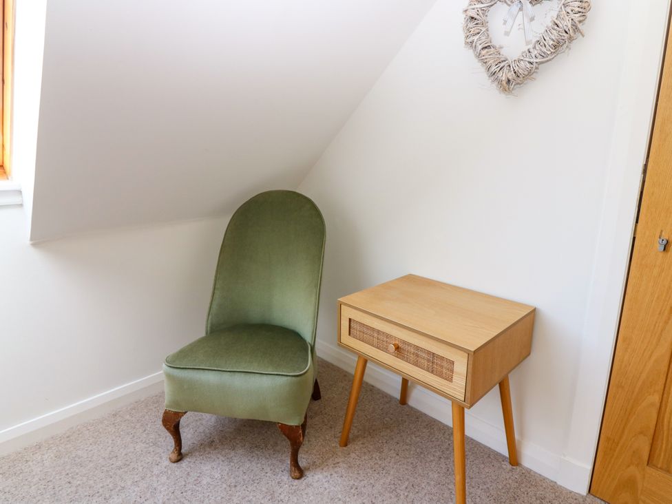 A bedroom with a green chair and wooden nightstand at Whitehouse Woodwrae in Aberlemno near Forfar