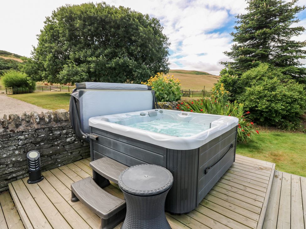A hot tub on a wooden deck with steps and furniture at Whitehouse Woodwrae Aberlemno near Forfar