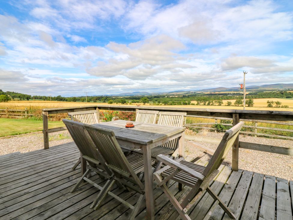 A deck with a wooden table and chairs overlooking a landscape at Whitehouse Woodwrae Aberlemno near Forfar