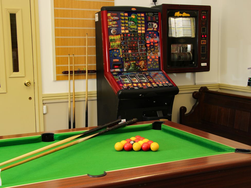 A pool table with billiard balls and cues beside a gaming machine and seating at The Boars Head Pub in Bishops Castle