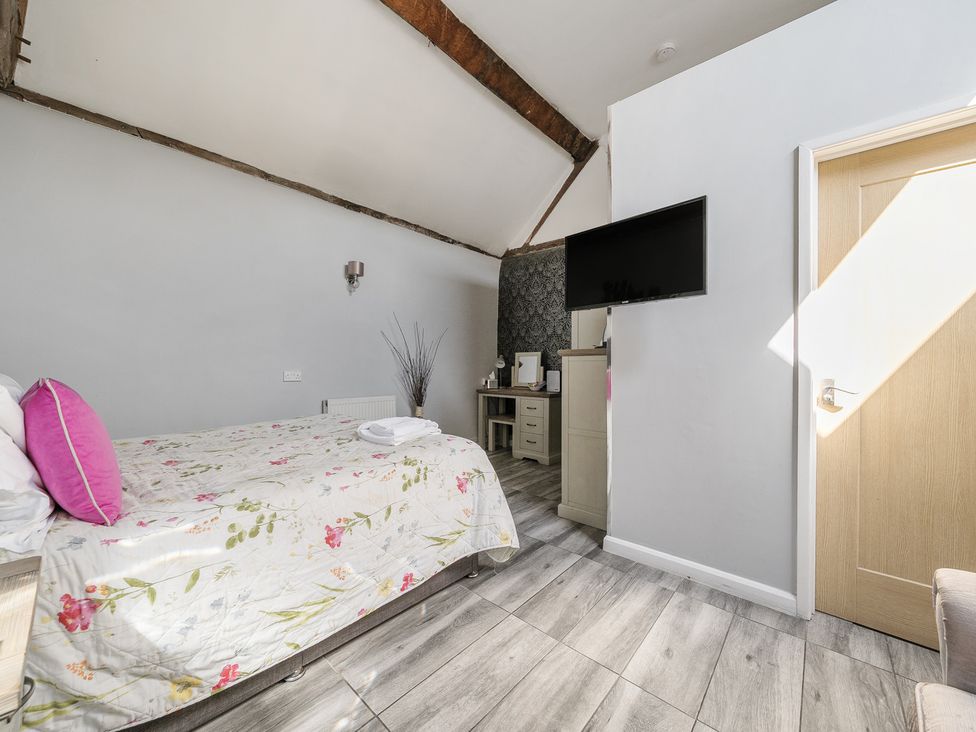 A bedroom with a bed and floral bedspread a wall-mounted tv and a wooden door at The Boars Head Pub in Bishop's Castle