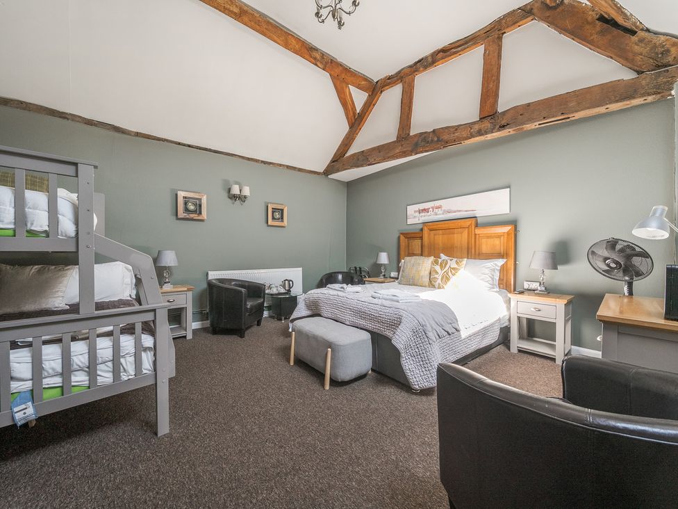 A bedroom with bunk beds armchairs a double bed side tables and wooden ceiling beams at The Boars Head Pub in Bishops Castle