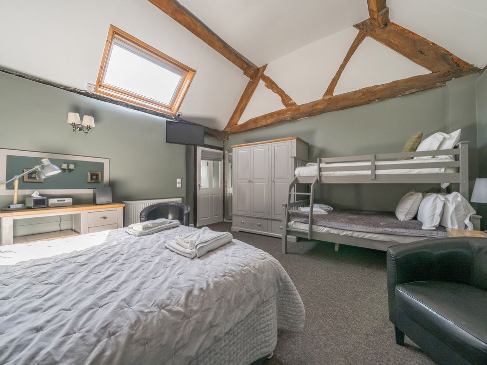 A bedroom with a double bed, bunk beds, wardrobe, desk, black chair, carpet, and exposed wooden beams at The Boars Head Pub in Bishops Castle