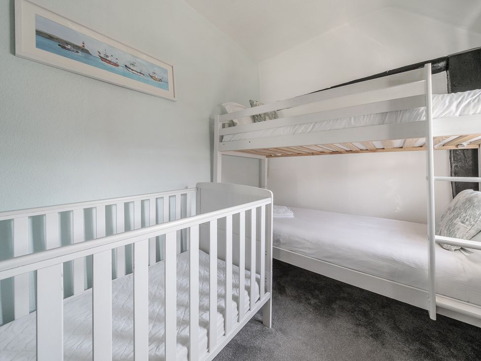 A bedroom with a white crib and white bunk beds with pillows and a wall painting of boats at The Boars Head Pub in Bishops Castle