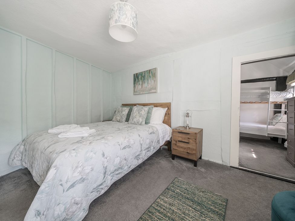 A bedroom with a double bed bedside table and open doorway showing bunk beds at The Boars Head Pub in Bishops Castle