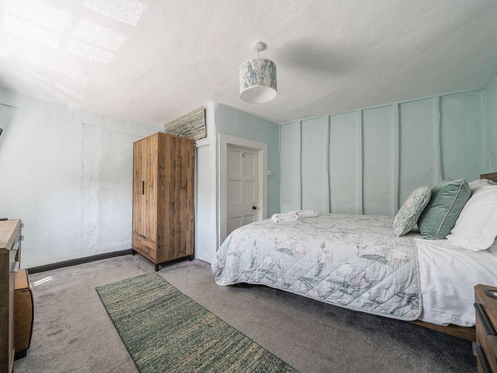 A bedroom with a bed with pillows and blanket a wooden wardrobe a rug and a door at The Boars Head Pub in Bishop's Castle