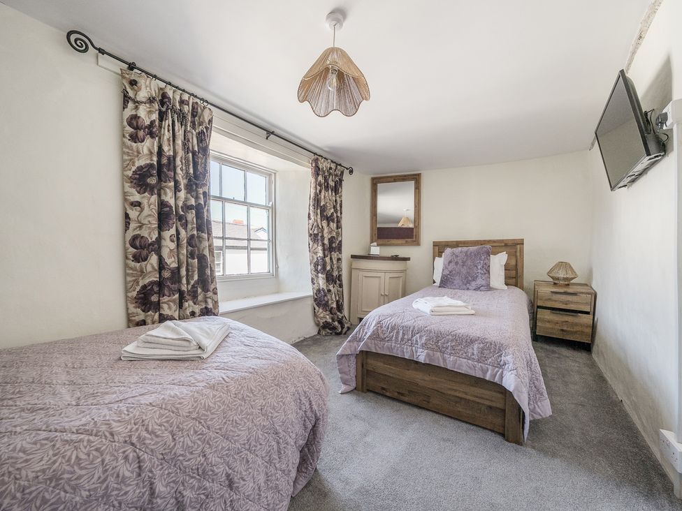 A bedroom with two single beds a window with floral curtains a wall-mounted tv and a wooden nightstand at The Boars Head Pub in Bishops Castle