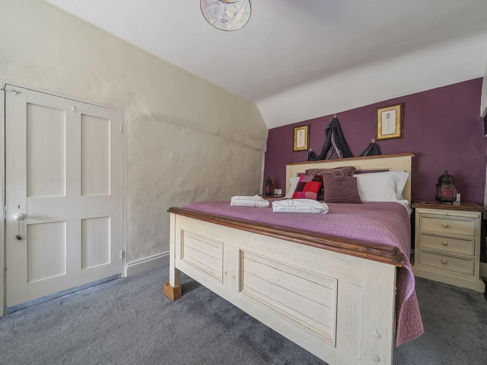 A bedroom with a wooden bed a purple bedspread bedside tables and framed pictures on a purple wall at The Boars Head Pub in Bishop's Castle