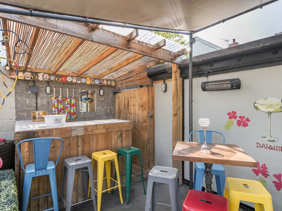 An outdoor bar area with wooden bar counter metal stools and a small wooden table with stools at The Boars Head Pub in Bishops Castle