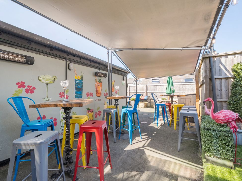 An outdoor seating area with colorful metal stools and wooden tables under a canopy with wall art of cocktails and a pink flamingo decoration at The Boars Head Pub in Bishops Castle