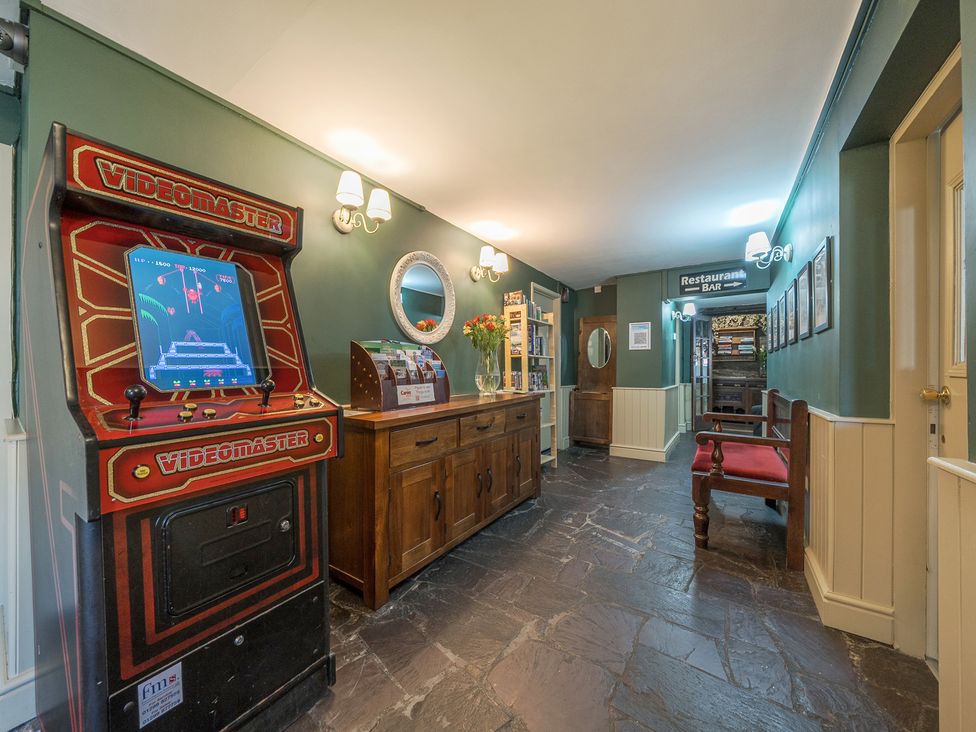 A hallway with a vintage videogame machine a wooden sideboard a bench and a sign pointing to restaurant and bar at The Boars Head Pub in Bishops Castle