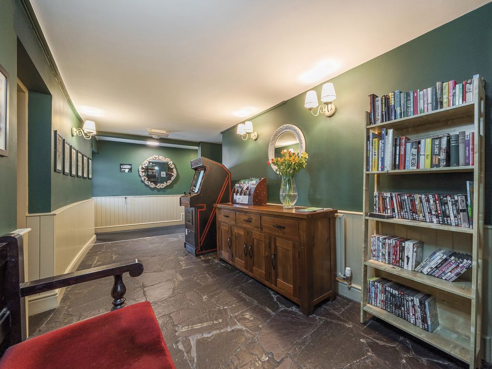 A hallway with green walls stone floor a wooden cabinet with flowers an arcade machine and a bookshelf at The Boars Head Pub in Bishops Castle