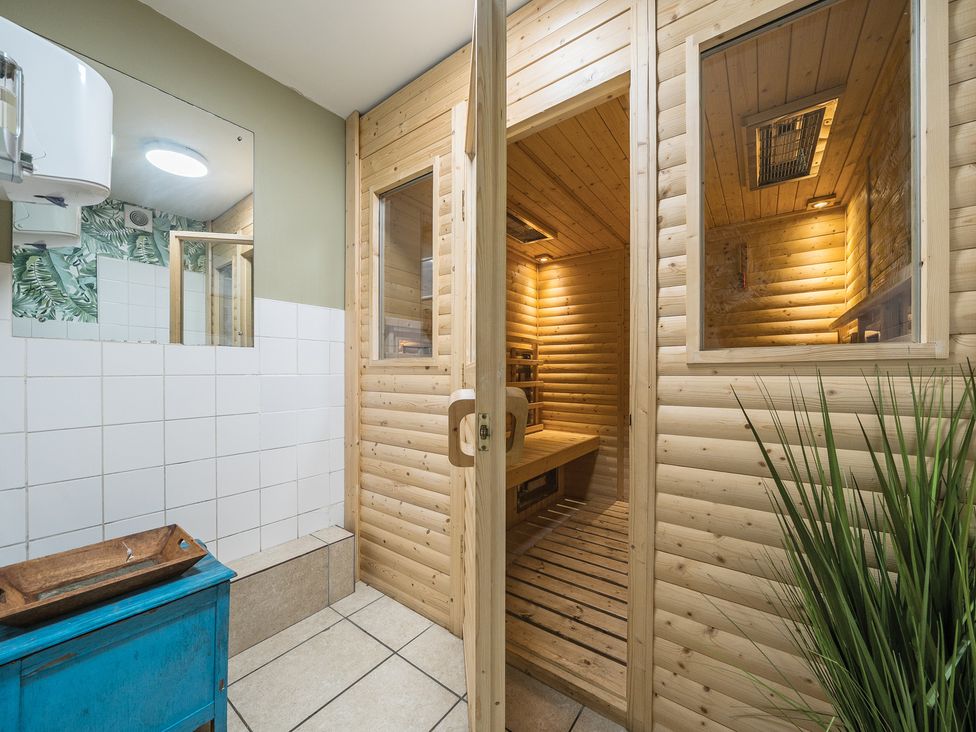 A wooden sauna room with an open door next to a tiled wall and a blue cabinet with a wooden tray at The Boars Head Pub in Bishops Castle