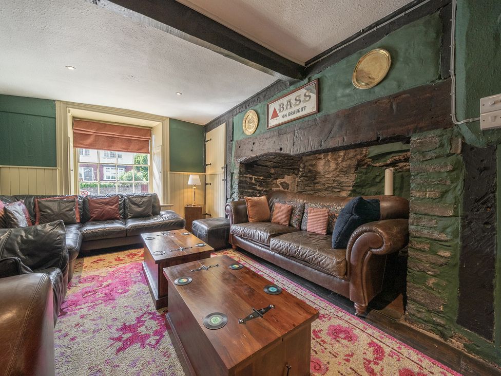 A sitting room with leather sofas wooden tables and a decorated stone fireplace at The Boars Head Pub in Bishop's Castle