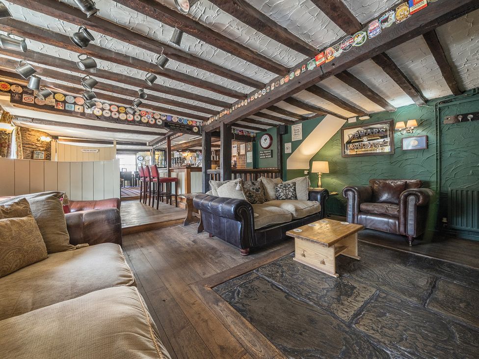 A pub seating area with sofas, armchairs, wooden tables, and a bar in the background at The Boars Head Pub in Bishops Castle