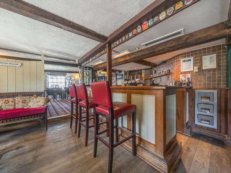 A bar area with red stools wooden floor and a seating area at The Boars Head Pub in Bishop's Castle