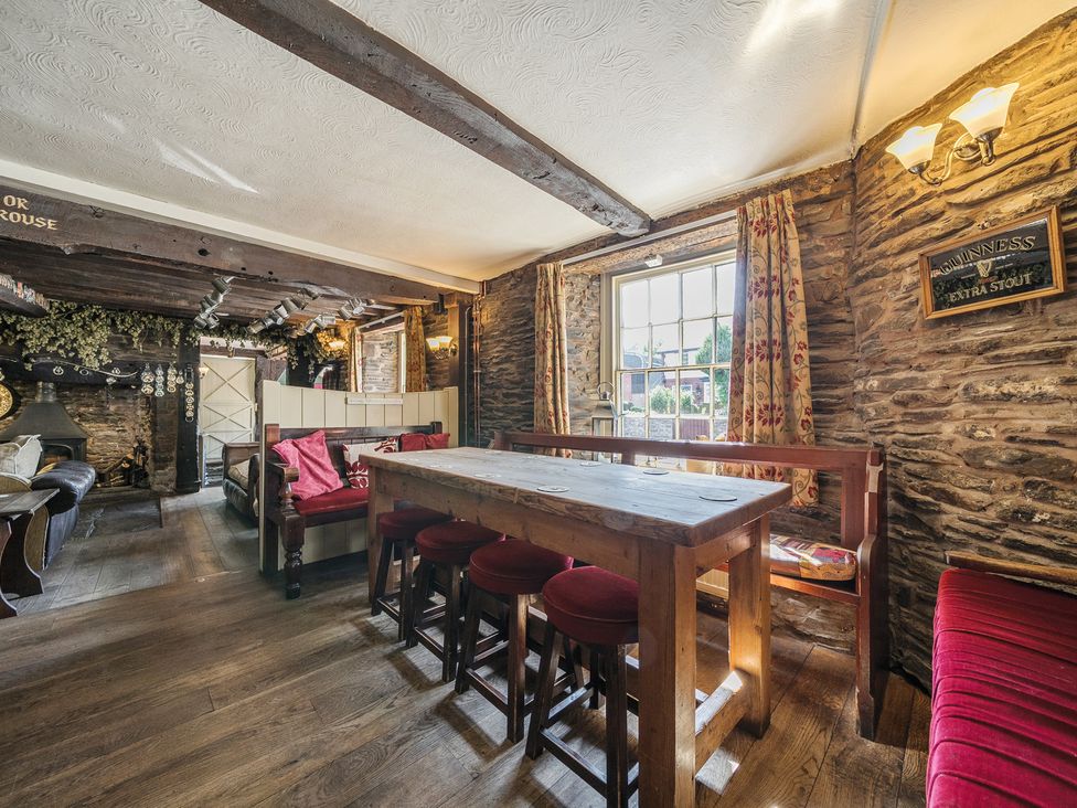A rustic pub interior with wooden tables and stools against a stone wall with a window at The Boars Head Pub in Bishop's Castle
