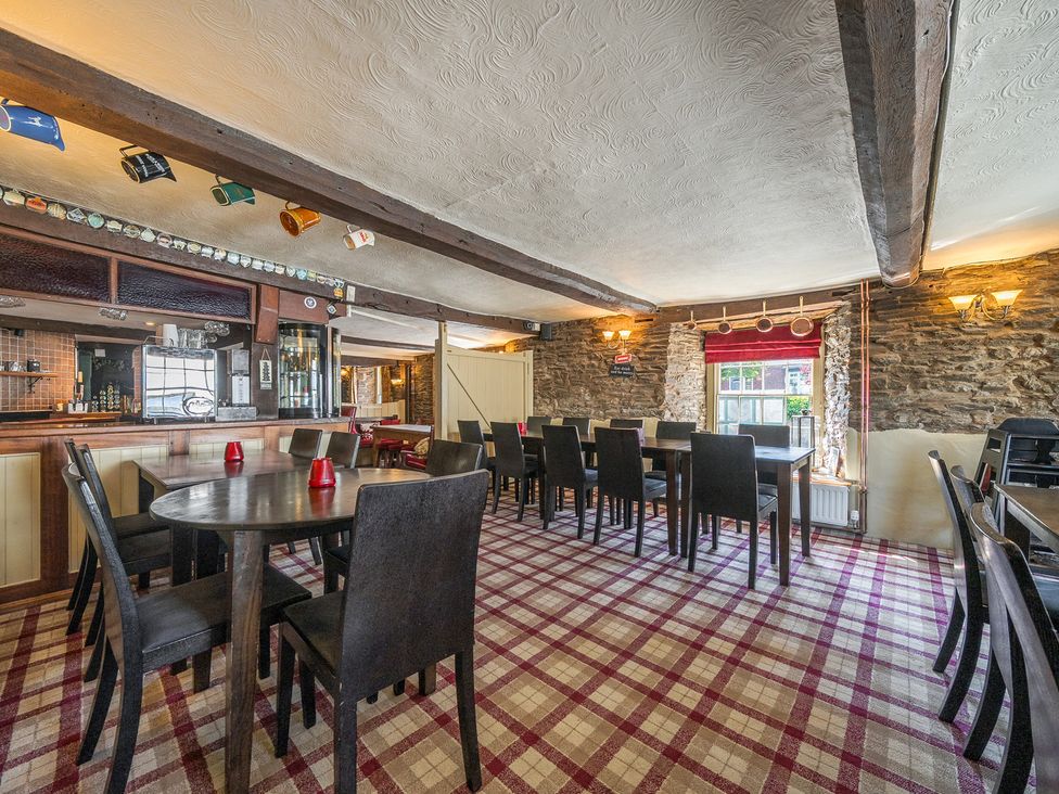 A dining area with dark wooden tables and chairs a bar counter stone walls and plaid carpet at The Boars Head Pub in Bishops Castle