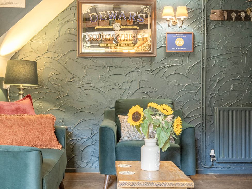 A sitting room with a green wall, sofa, flower vase, and an award plaque at The Boars Head Pub, Bishop's Castle