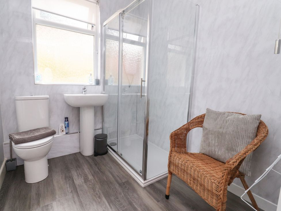 A bathroom with a shower, sink, toilet and a chair at Cosy Bee in Heysham
